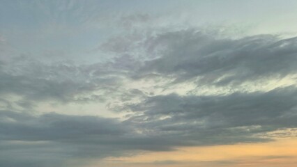 Obraz premium Dramatic Grey Clouds Stretching Across a Calm Sunset Sky at the Golden Horizon