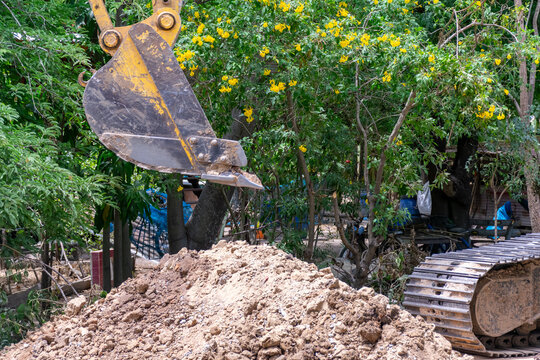 Heavy excavator bucket crawler track beside large soil pile during earthmoving work green outdoor construction area