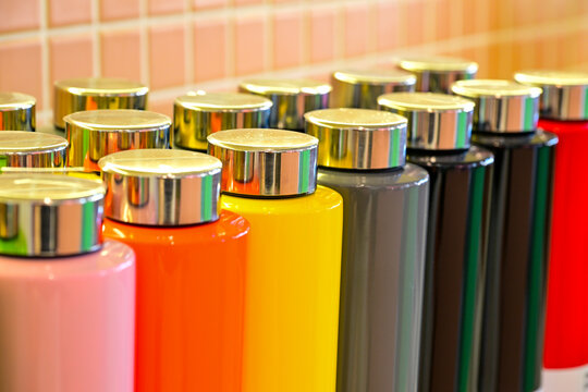 A lot of  plastic color thermos mugs on yellow  background with copy space; selective focus.  Multi Color thermos mugs on the white wooden table, over white background. Acrylic paints of different col