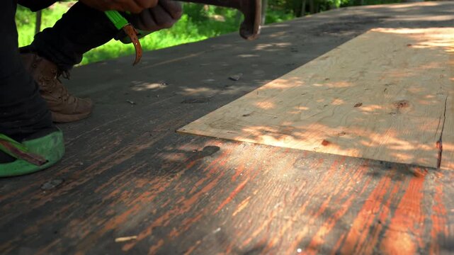 Close up of a roofing contractor worker hammering nails into plywood roof sheathing during a residential roof replacement process.