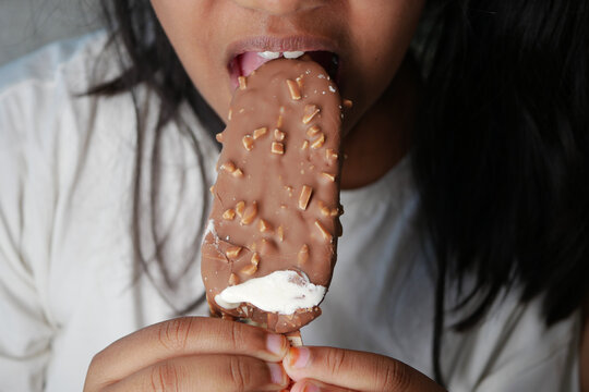 A child is biting into a chocolate ice cream bar with crunchy bits
