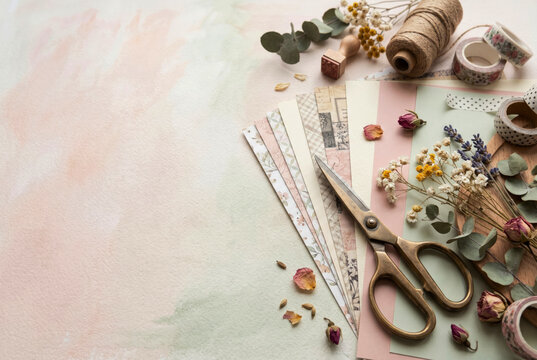 Scrapbook materials, decorative paper, dried flowers and scissors arranged on a soft pastel background for handmade projects. Paper crafts, memory keeping and creative hobby concept. Copy space