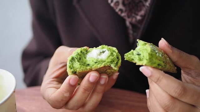holding a split green-colored baked snack, such as a spinach or matcha muffin with a cream cheese or yogurt filling