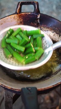 Cooking Thai vegetables with shrimp paste dip. Blanching ivy gourd leaves, angled gourd, and okra in hot water, pounding chilies, garlic, and shrimp paste in mortar, served together as a healthy Thai 