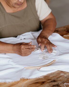 Close up of a Zapotec womans weathered hands unpicking embroidery at a timber table for a slow craft and traditional textile campaign