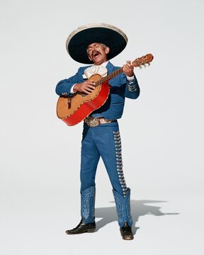 A mariachi musician in a blue embroidered suit singing and playing a red guitar against a white background for cultural event promotion and advertising
