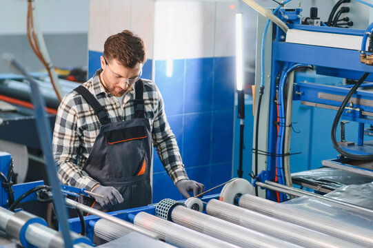 Worker wearing safety glasses operating plastic bag production machine