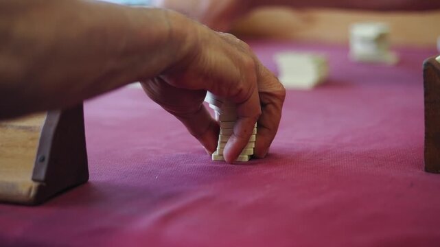 Senior Person Playing Rummy Tile Game on Red Table