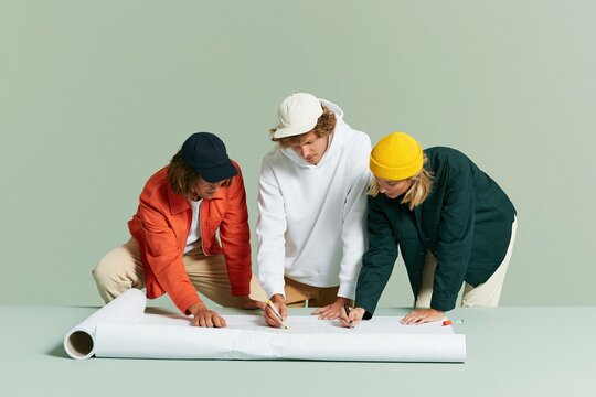 Three young people collaborating on a large paper floor plan for event planning and project management, showing creative teamwork in a bright studio