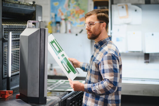 Printing press operator checking print quality in workshop