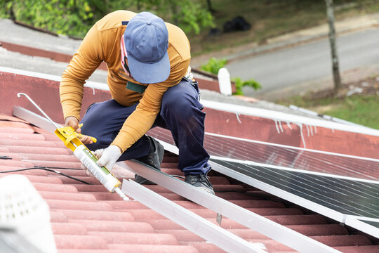 Worker installing mounting brackets onto red residential roof for solar photovoltaic or PV panels in Malaysia