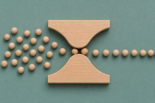 Wooden beads move through narrowing hourglass pathway, illustrating business bottleneck, workflow constraints, process delays, operational inefficiency and restricted productivity in minimalist flat l