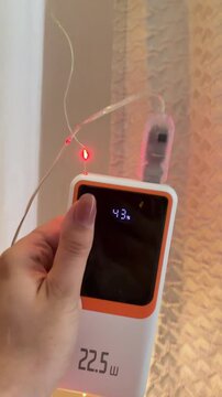 Woman holding a portable power bank powering a glowing decorative string of colorful fairy lights for festive home holiday illumination and vibrant party ambiance