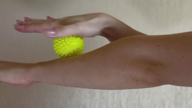 Woman massaging her arm with a spiky stress ball for myofascial release, muscle pain relief, and physical therapy recovery. Self care routine for forearm tension and soreness