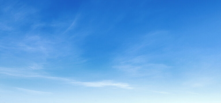 Soft clouds drift across a vast, serene blue sky
