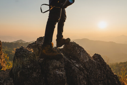 Hiker stands atop rugged rock, backlit by golden sun