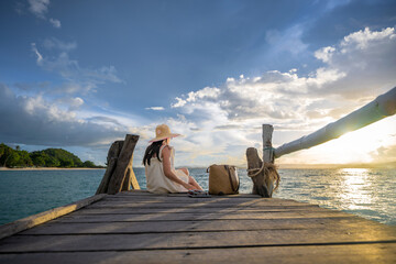 Fototapeta premium Woman tourist in moment easy going and relax on wooden pier, enjoy sunset of the summer trip in Koh Thalu island locate in Prachaup province,THAILAND
