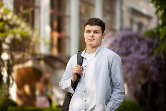 Young man stands in front of university building with backpack during spring day in city