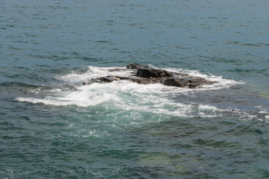 Sea waves crashing over dark rocky reef in clear ocean water