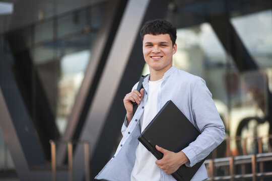 Young man stands outside building with laptop in hand, ready for work or study in urban setting