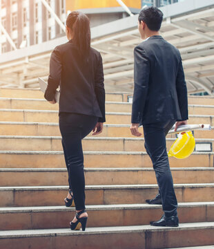 Business and success concept. Persons Back view walking toward successful after meeting. Legs of Engineer and Businesswoman Walk up stairway together to progress work in office-vertical image.