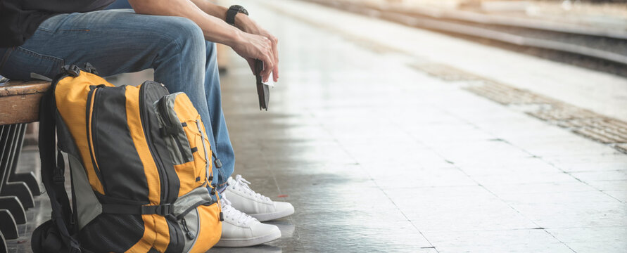 At train station, Asian Backpacker waiting train and planning happy holiday vacation. Young Tourist man searching right direction. Travel concept-banner image.