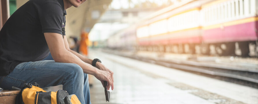 At train station, Asian Backpacker waiting train and planning happy holiday vacation. Young Tourist man searching right direction. Travel concept-banner image.