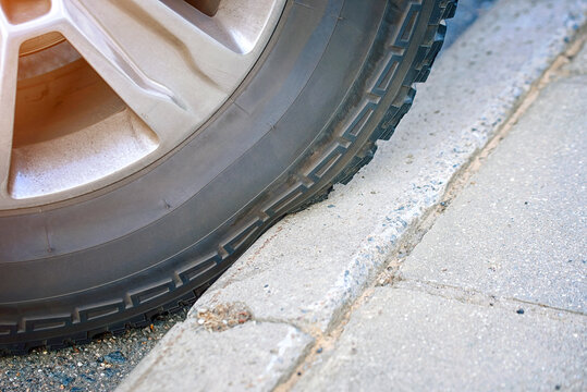 Car black rubber tire and alloy wheel rim pressed tightly against edge of concrete sidewalk curb during urban parking. Car rubber tire sidewall squeezed against concrete curb edge. Selective focus