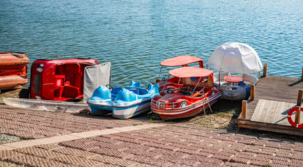 Colorful pedal boats docked at pier on calm lake, water recreation concept © Ployker