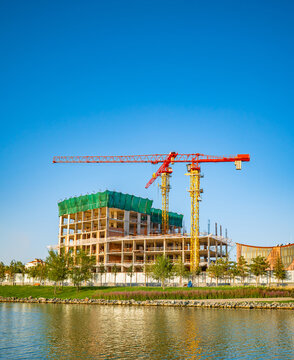 Modern building under construction with crane next to lake, urban development concept