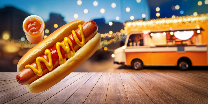 Hot dog with mustard and ketchup on a wooden table with blurred food truck background and copy space