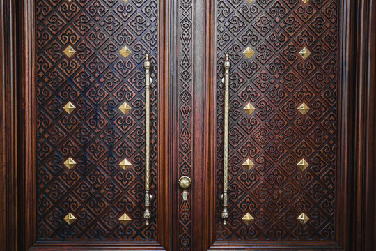 Ornate carved dark wooden double door with golden brass studs in mosque, traditional Islamic architecture concept