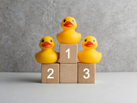 Three yellow rubber duck toys stacked on numbered wooden blocks for learning and play