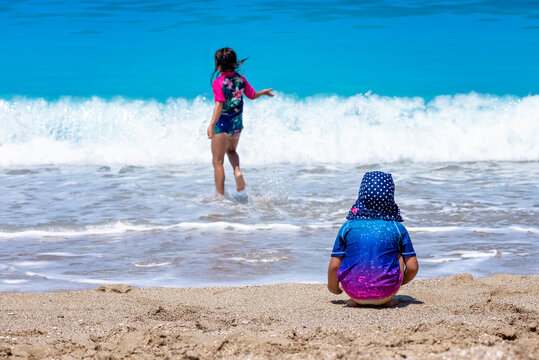 girls palying on the beach wearing sun protective clothes, two sisters enjoying hot summer day on the beach 