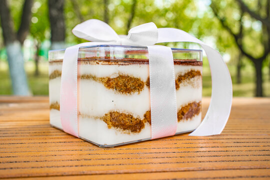 Tiramisu dessert portion wrapped with white ribbon bow on wooden surface, Italian pastry gift concept