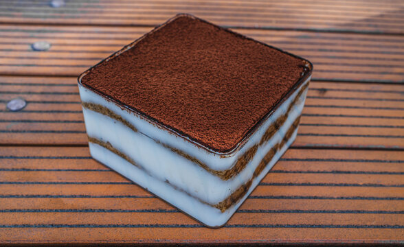 Single tiramisu dessert portion with cocoa powder top on wooden surface, Italian pastry and food concept