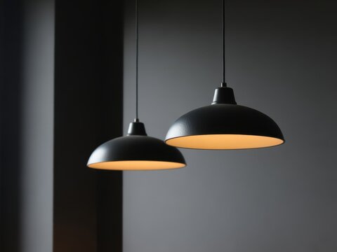 Two modern matte black pendant lamps hanging from the ceiling against a dark grey wall, providing warm soft interior lighting in a minimalist contemporary room style