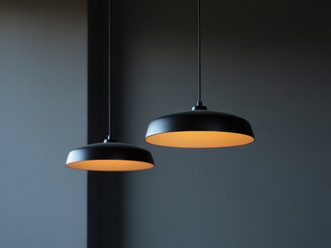 Two modern minimalist pendant lamps with black metal shades and warm glowing light, hanging from ceiling in a dark room, contemporary interior lighting fixture