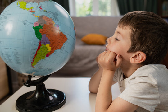 boy studies a globe and looks at a world map at home at the table. Early preschool development. Citizens of the world, a world without borders, globalization.