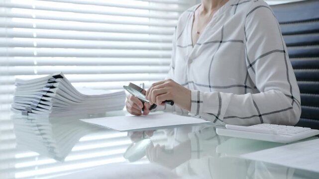 Woman's hands using a calculator and holding a pen, working with financial documents and a pile of papers on a clear desk in an office setup