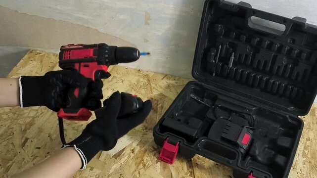 Mechanic connecting battery to cordless screwdriver and turning it on in workshop, power tools, repair, construction and maintenance concept.