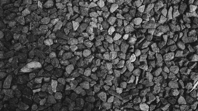 Monochrome close-up of dark gravel stones with varied shapes and natural textures, suitable as a rustic stone, ground or abstract background