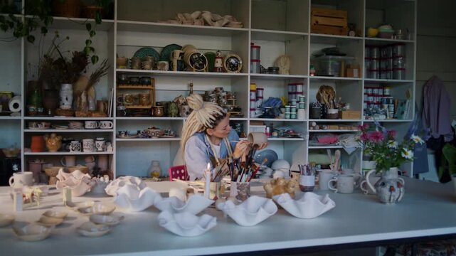 Woman creates ceramic piece at table in spacious pottery studio