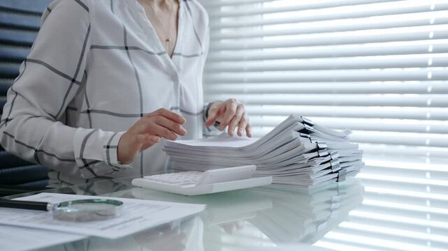 Financial professional calculating expenses and managing a large workload of business documents, analyzing reports, and organizing paperwork in an office setting