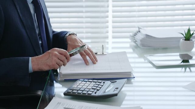 Professional auditor analyzing financial data with a magnifying glass, performing a detailed business investigation, checking documents, and verifying accounting records at the desk