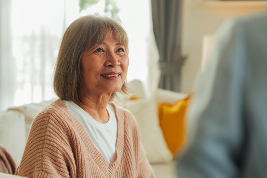 A close-up portrait of a smiling elderly woman gazing upward with warmth, a caregiver's sleeve softly blurred in the foreground an intimate depiction of comfort, contentment, and companionship at home