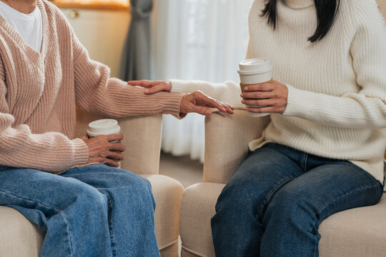 A mother and daughter sit facing each other with coffee cups in hand, engaged in heartfelt conversation as a hand reaches toward the other on the armrest an intimate moment of listening and connection