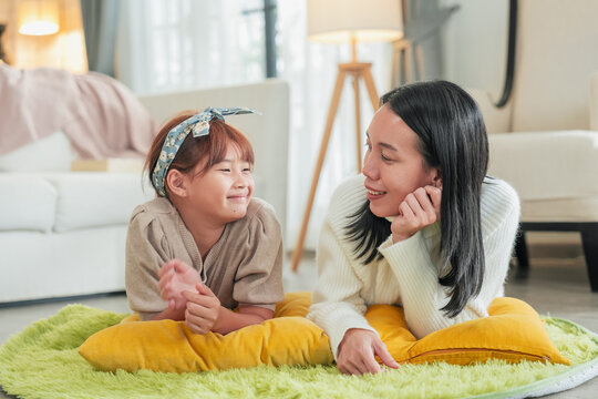 A mother and young daughter lie face to face on a cozy floor rug, hands clasped as they share a warm, giggly conversation intimate portrait of maternal bonding, trust, and quality time at home