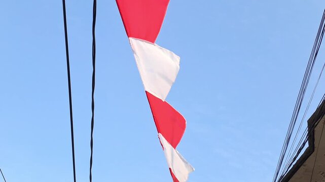 Red and white pennant flags hanging in residential area for Indonesia Independence Day. Blue sky, 17 August celebration, national holiday, patriotic.