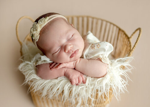 Newborn girl sleeping peacefully in a woven basket.